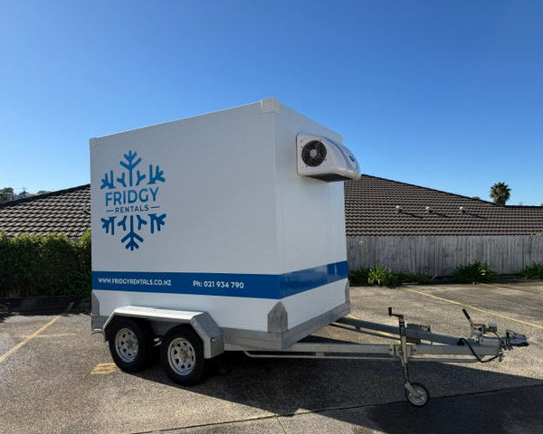 Extra large Fridgy Rentals trailer, white with a blue stripe and the snowflake logo, parked outdoors